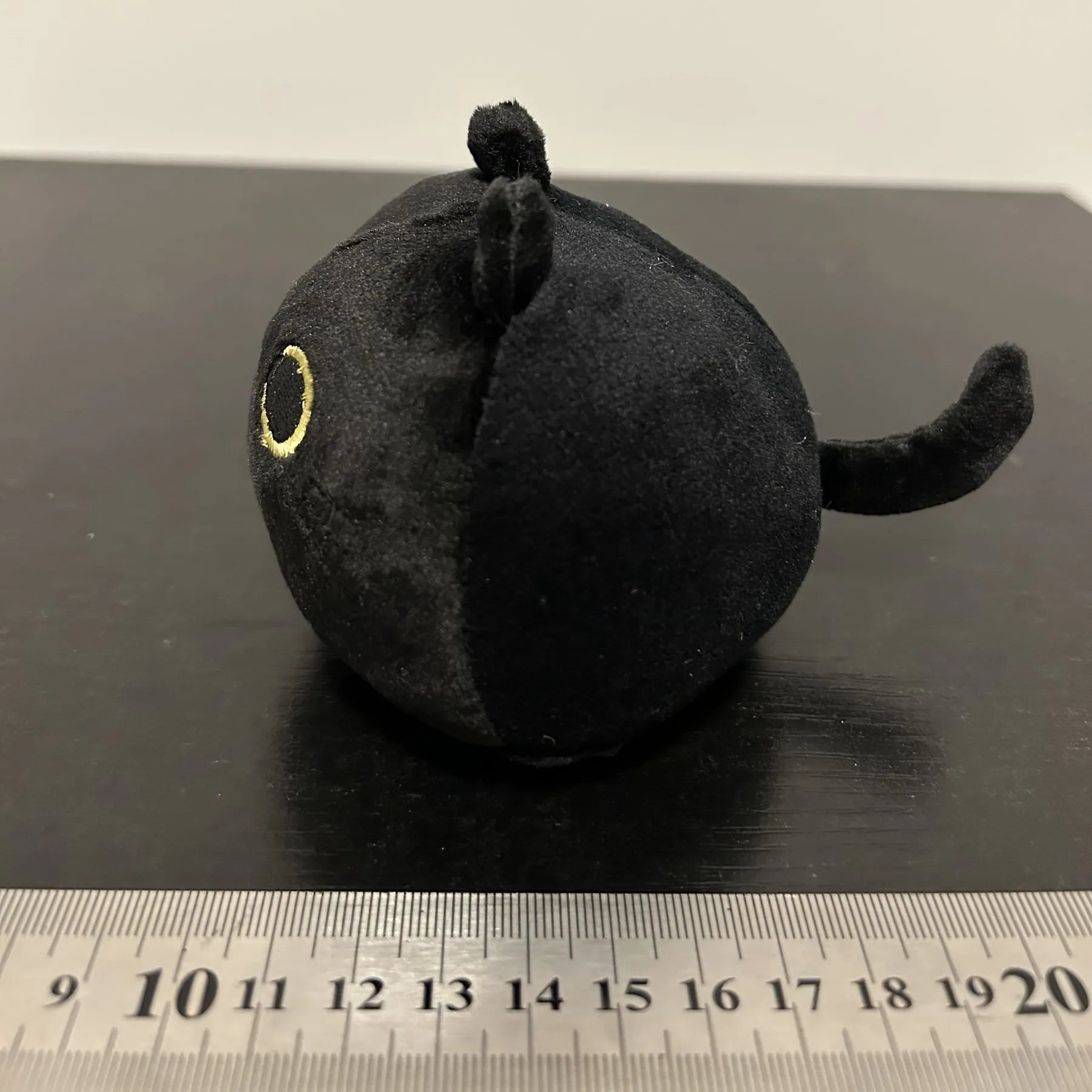 Fluffy black cat stuffed toy with embroidered eyes and whiskers on a grey background.