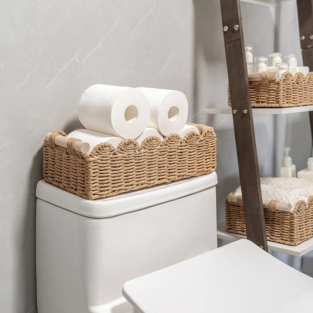 A woven paper storage basket in a neutral colour on a wooden desktop, holding remote controls and pens.