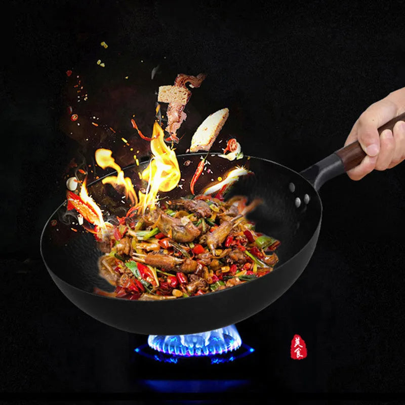 Traditional black iron wok pan with a wooden handle on a hob.