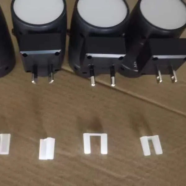 Small white plug-in night lamp with a rotatable light head on a bedside table.