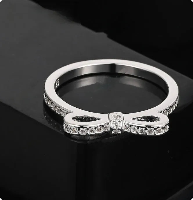 Silver colour bow-shaped ring with rhinestone and zircon crystal decoration on a finger.