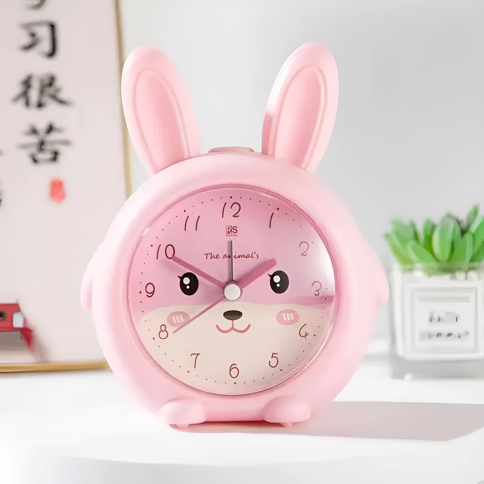 Pink and blue cartoon-style children's singing alarm clock with night light on a bedside table.