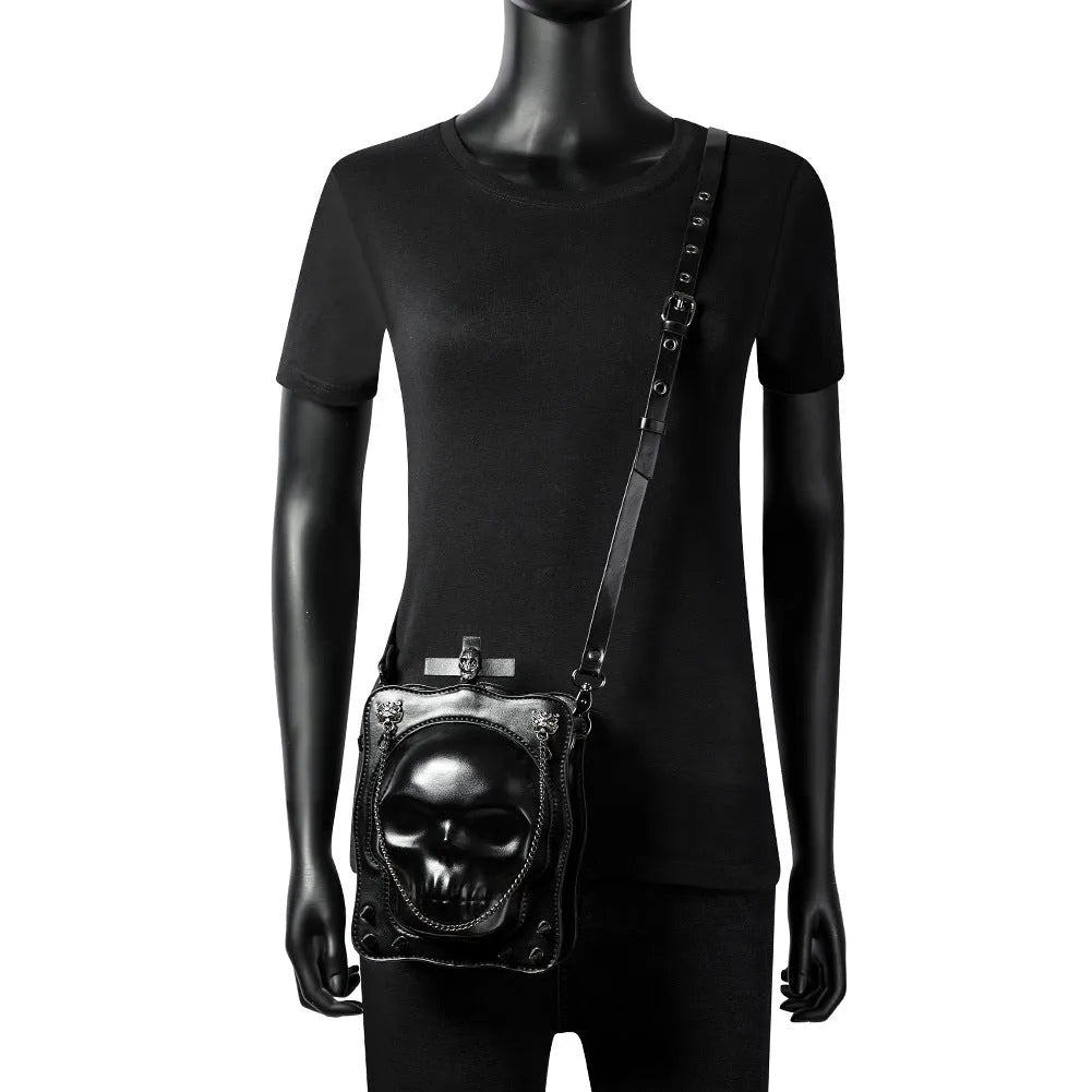 Black mini square crossbody bag with embossed skull design, metal chain strap, rivets, and contrast stitching.