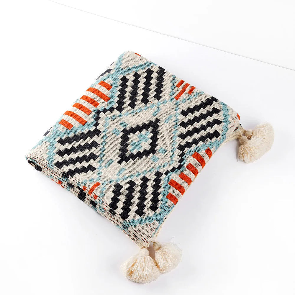 Bohemian style acrylic blanket with tassel fringe on a sofa, shown in a geometric print colour.