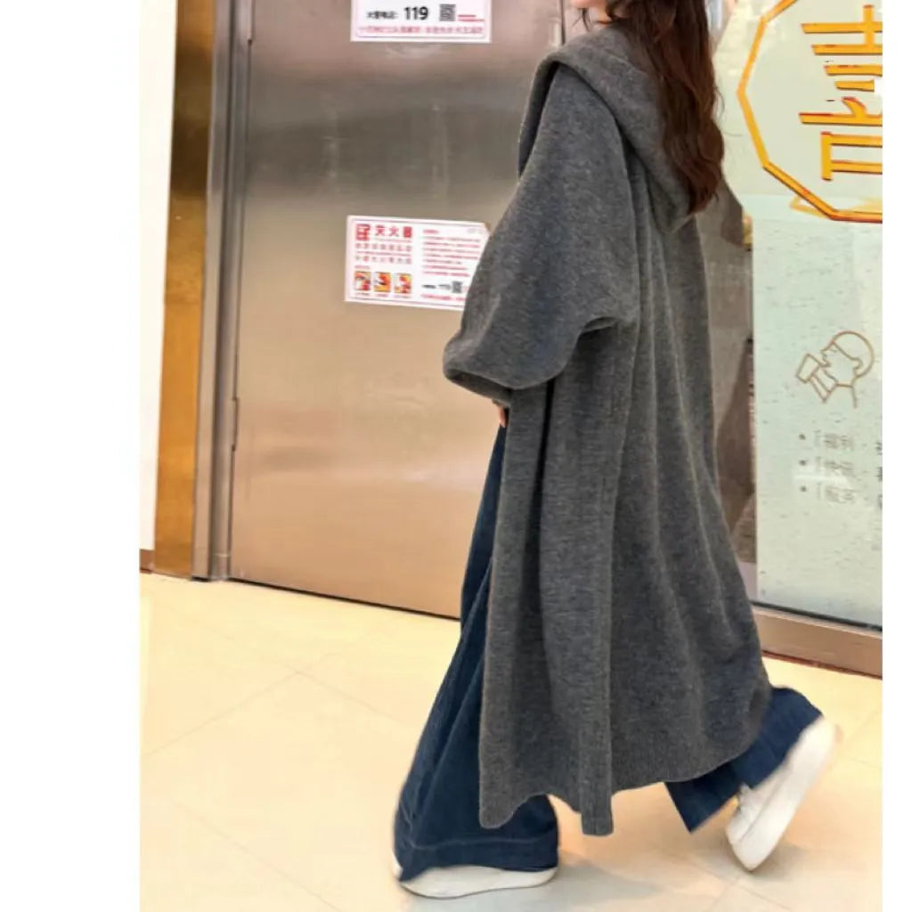 Women's long hooded knitted cardigan in oatmeal colour, showing below-knee length and loose fit.