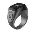 Zikr1 smart ring in silver on a charging cable next to its case, showing the OLED display.