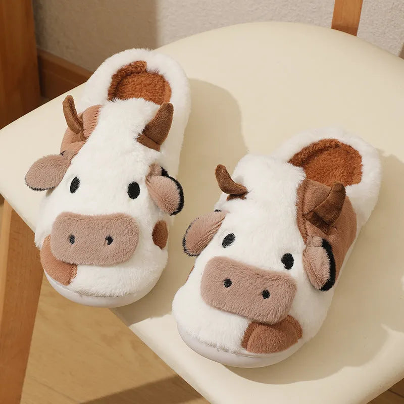 White cow-patterned plush slippers for women with a non-slip textured sole on a wooden floor