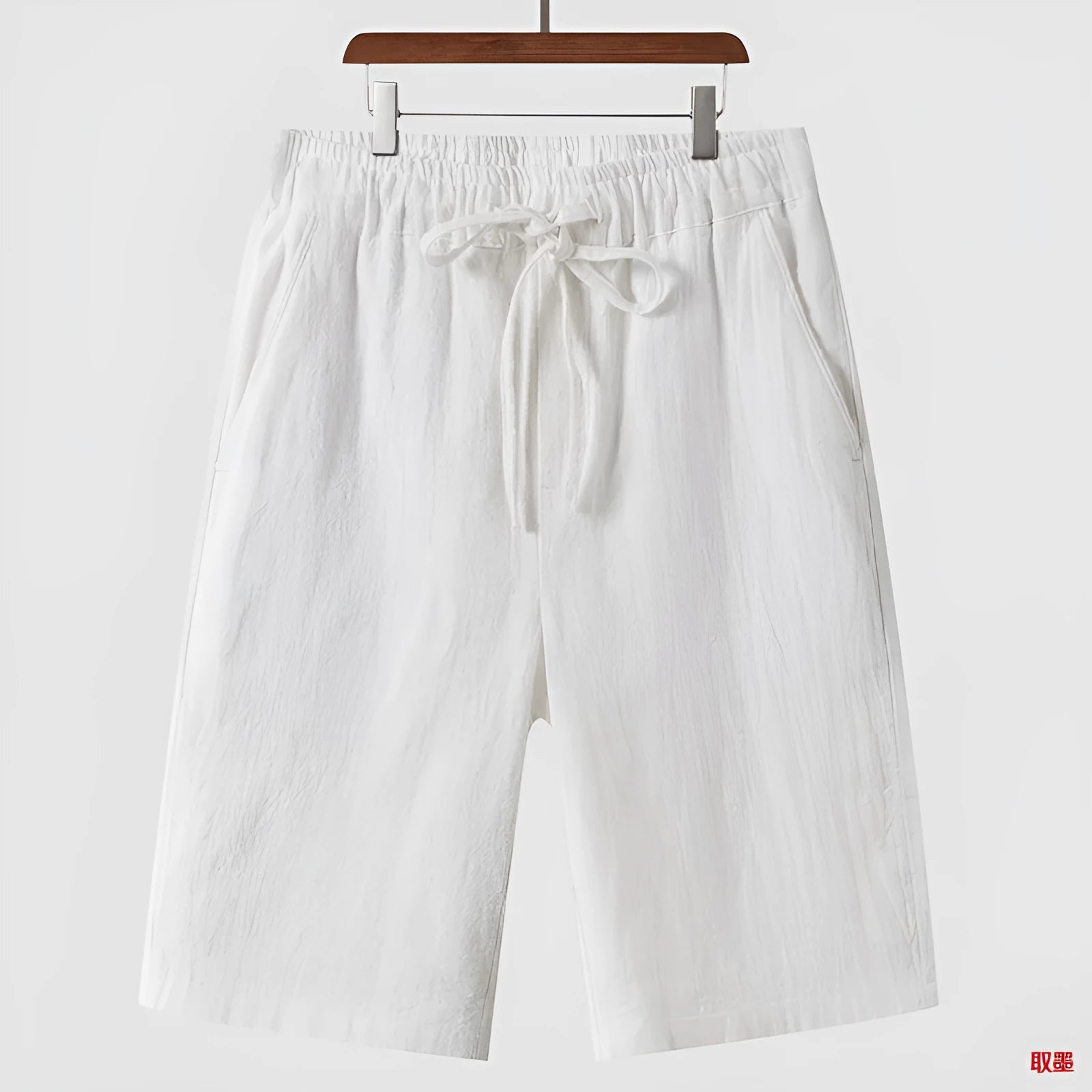 A pair of beige linen shorts for men with a loose, cropped fit and a mid-rise elasticated waistband.