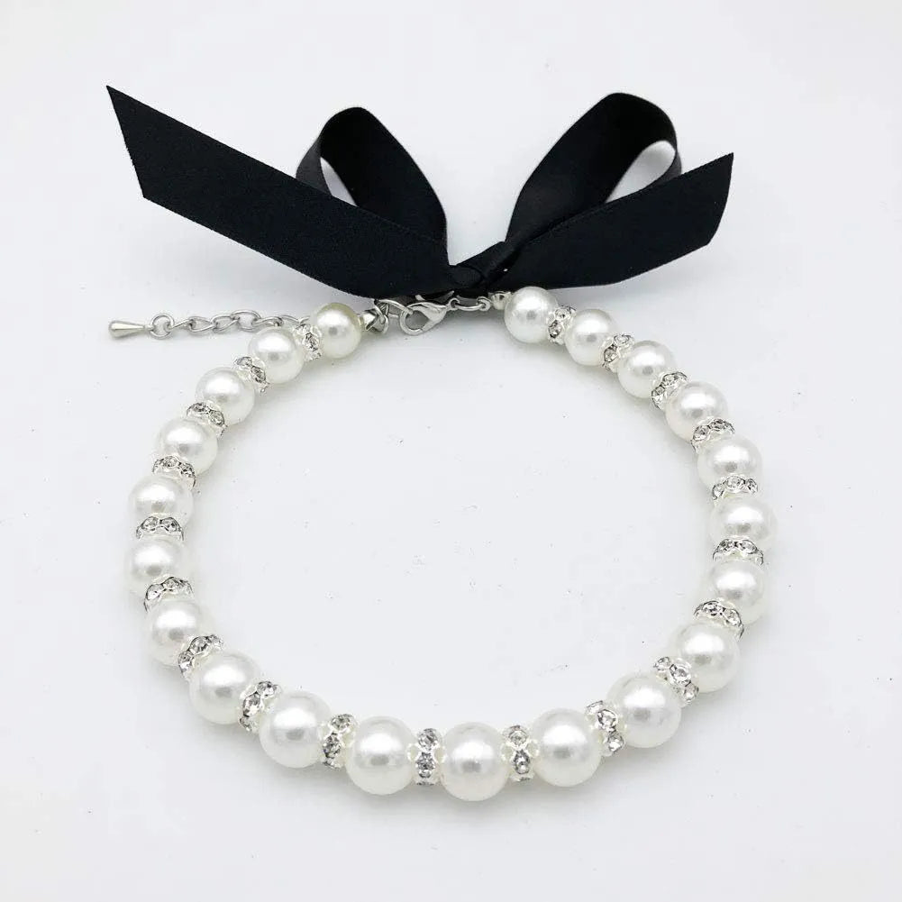 Small dog wearing a blue adjustable pearl and rhinestone necklace with a ribbon bow