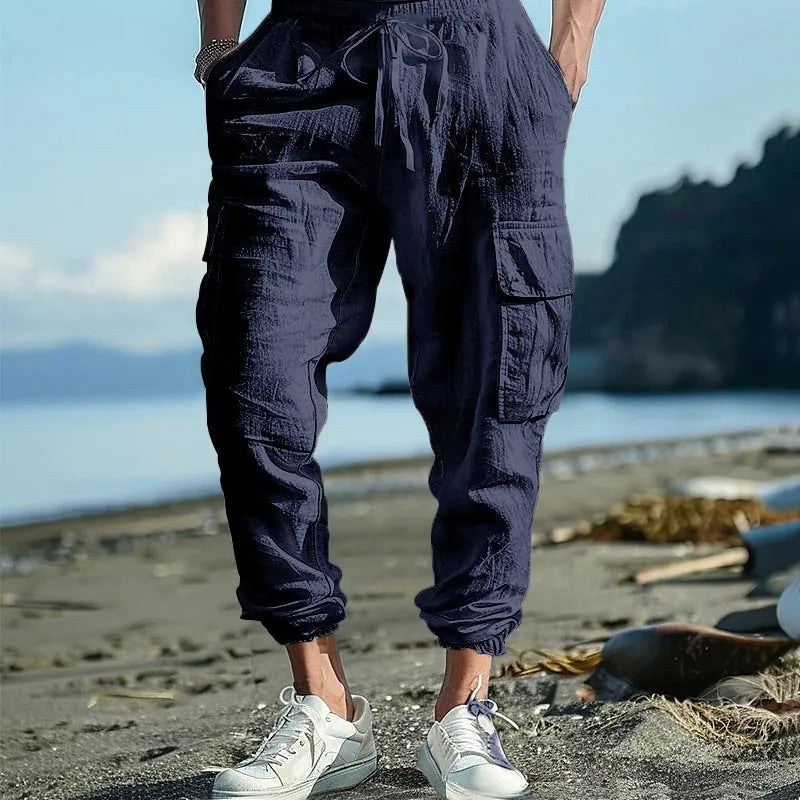 Man wearing loose-fit linen trousers with ankle-tied cuffs and a multi-pocket tether detail.