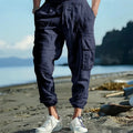 Man wearing loose-fit linen trousers with ankle-tied cuffs and a multi-pocket tether detail.