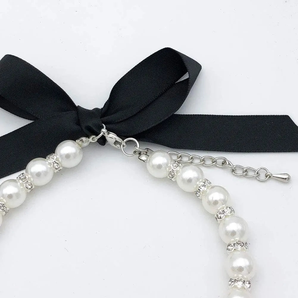 Small dog wearing a blue adjustable pearl and rhinestone necklace with a ribbon bow