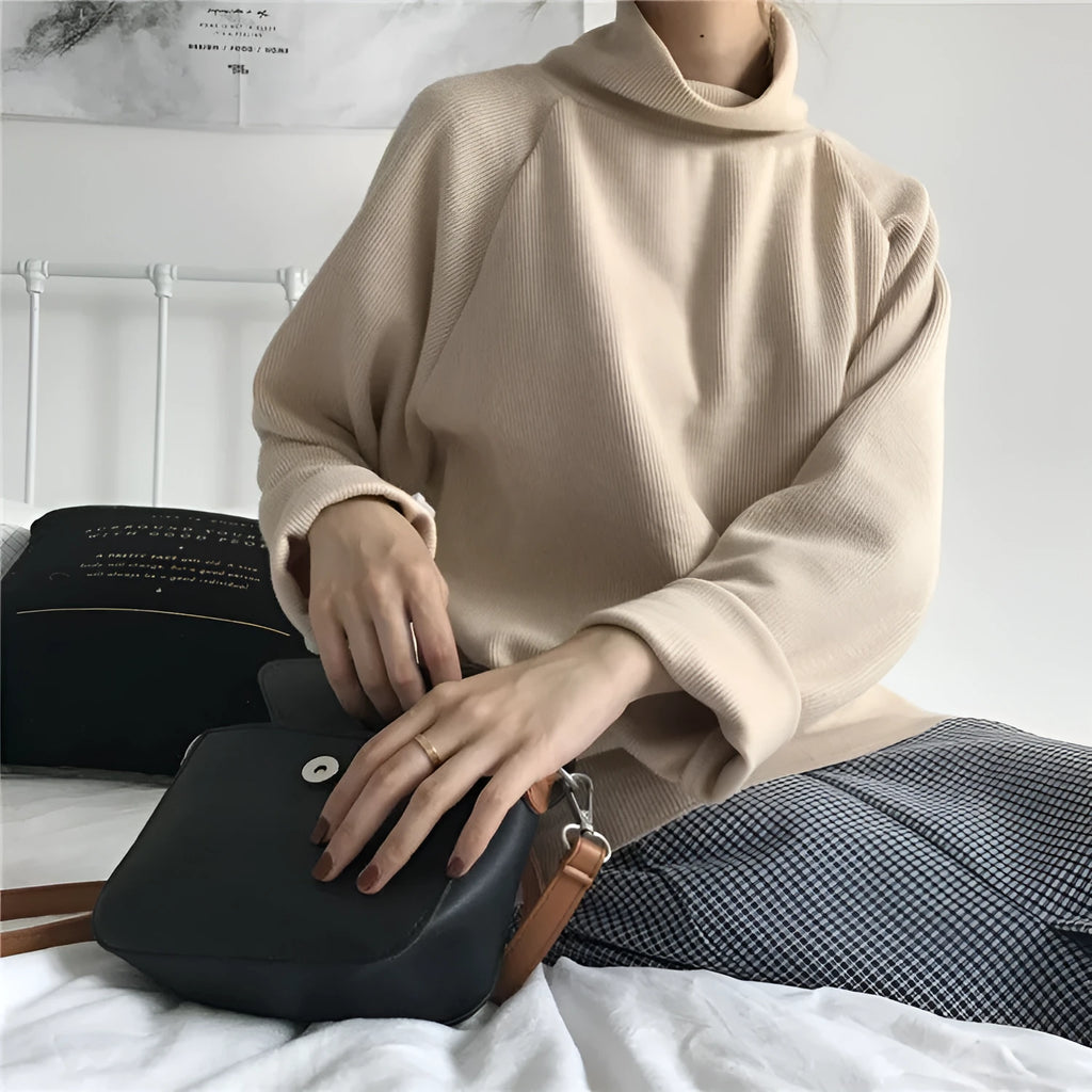 Woman wearing a solid apricot coloured loose fit long sleeve top with a half-high collar