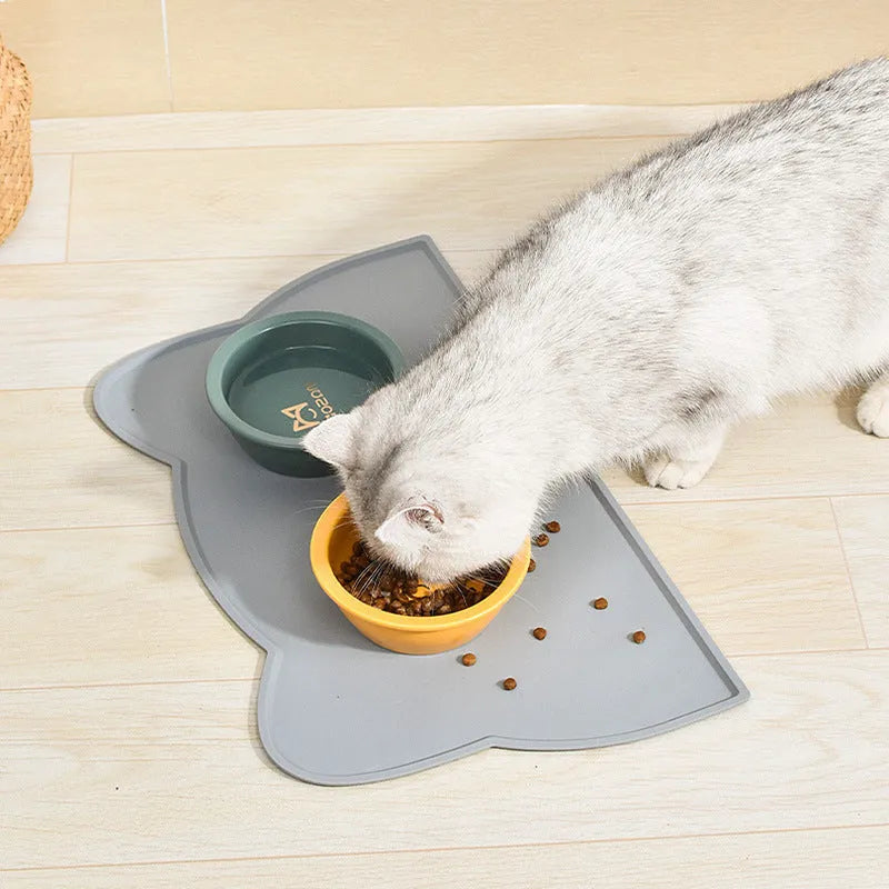 Blue silicone pet feeding mat with cat head shape under food and water bowls.