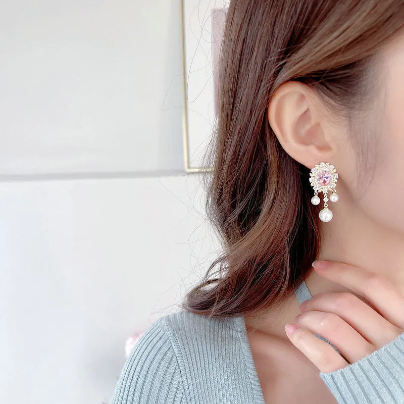 A pair of geometric ellipse-shaped drop earrings with a tassel, featuring pearls and inlaid zircon stones on copper.