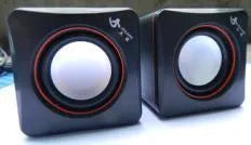 Small black square USB computer speaker on a desk next to a laptop.