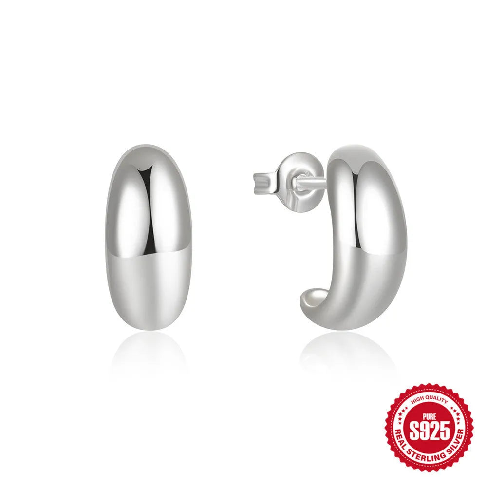 Close-up of a glossy C-shaped sterling silver stud earring in gold electroplated finish on a plain background.