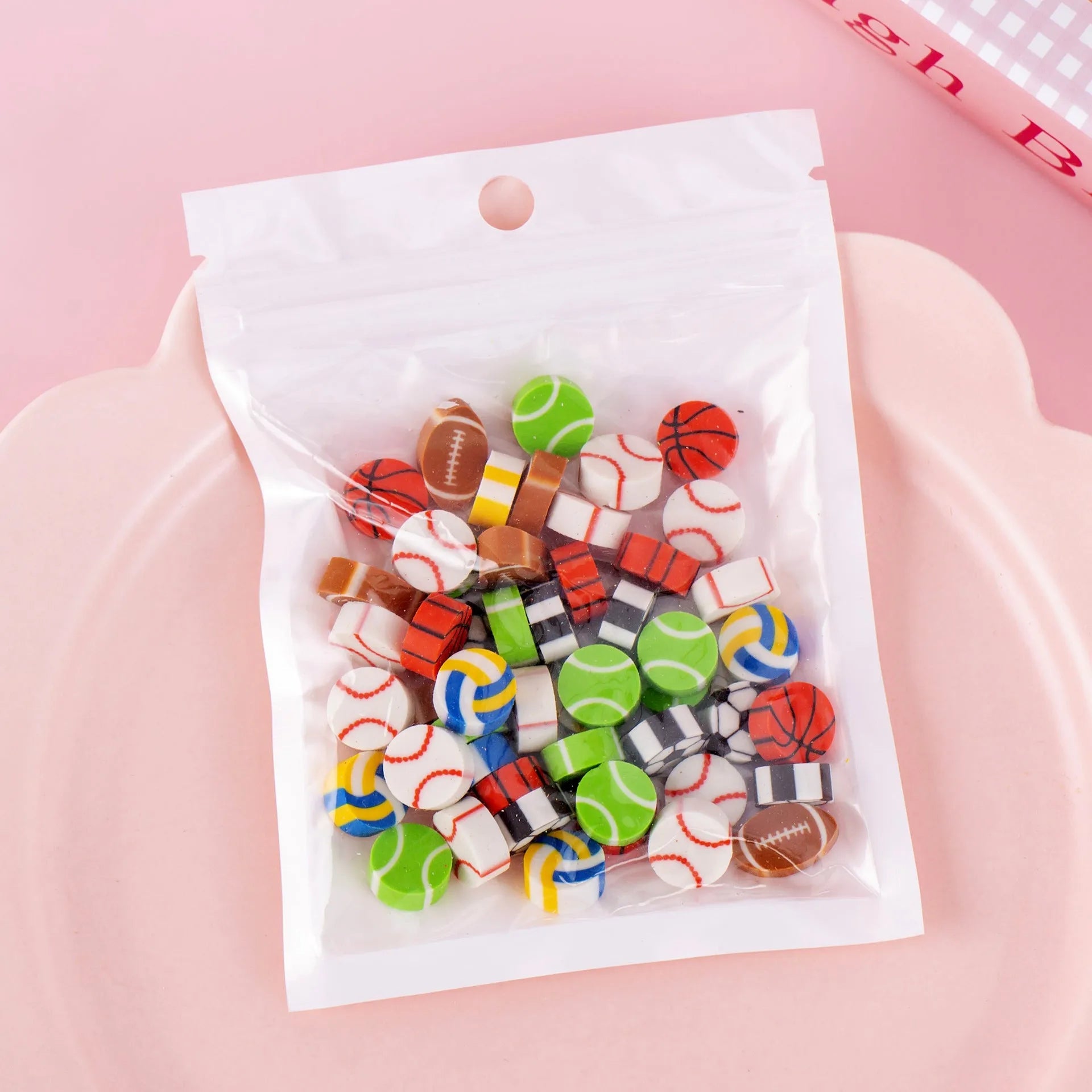 Open pearlescent film bag showing 50 small colourful cartoon fruit-themed rubber erasers.