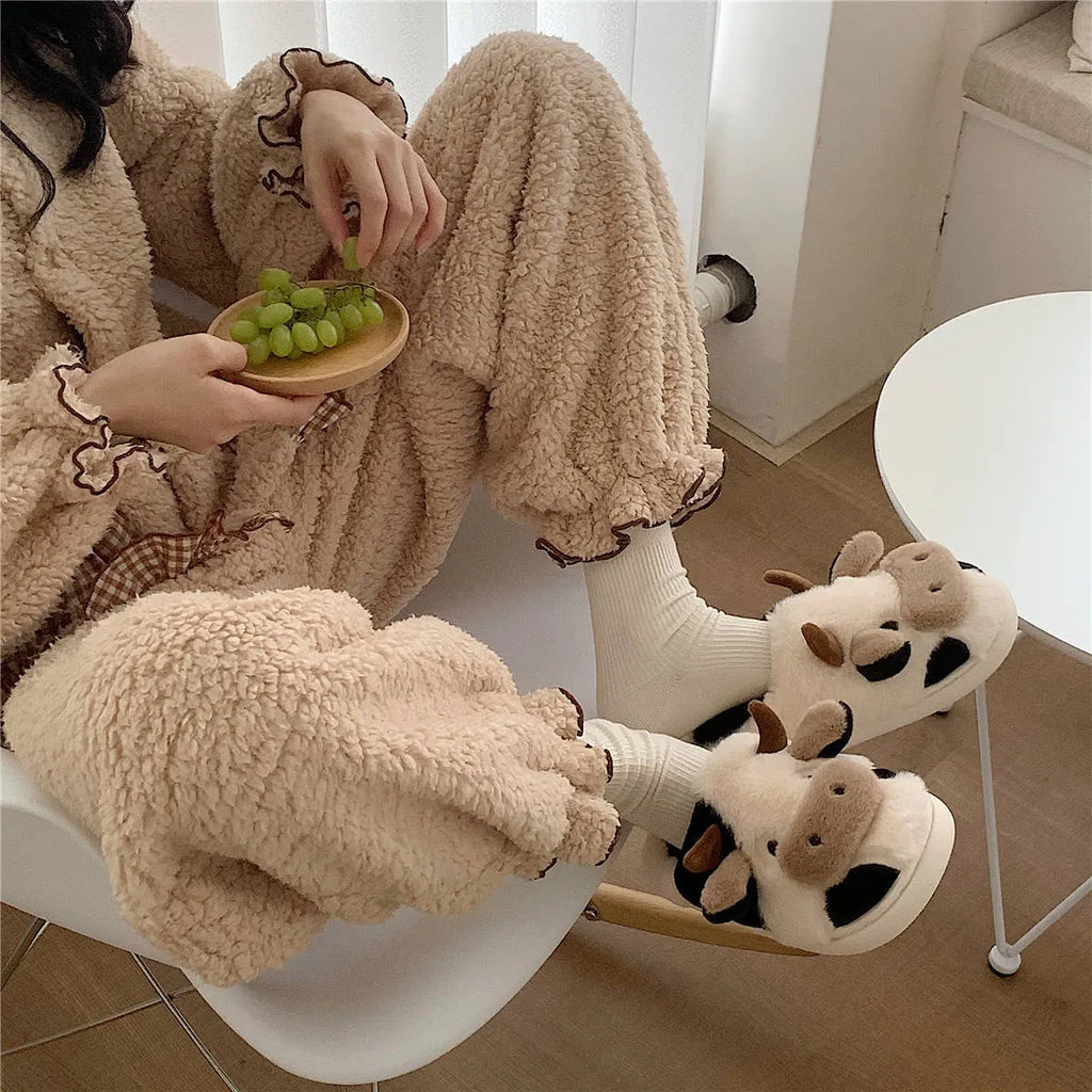 White cow-patterned plush slippers for women with a non-slip textured sole on a wooden floor