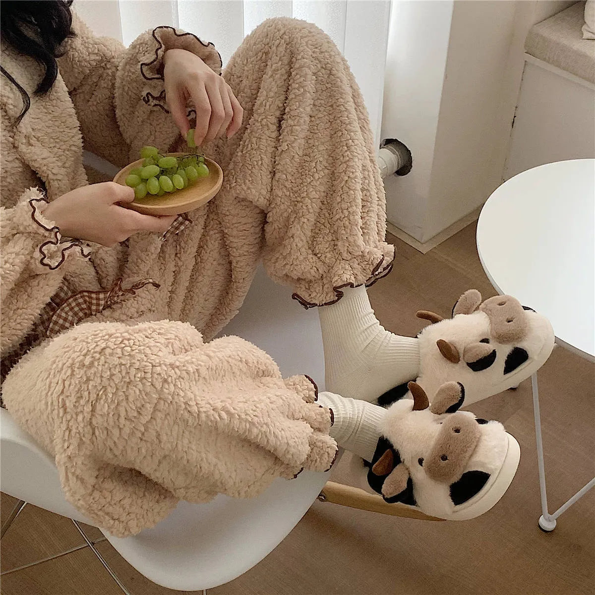 White cow-patterned plush slippers for women with a non-slip textured sole on a wooden floor
