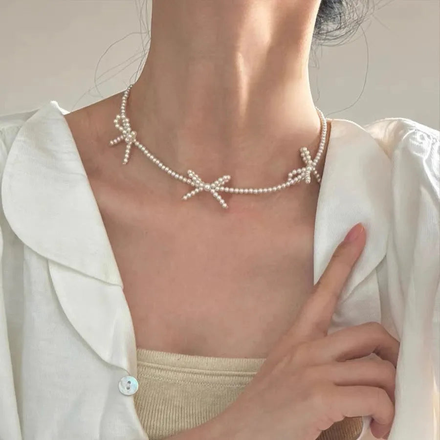 White imitation pearl necklace with a central bow pendant on a chain, adjustable from 31cm to 40cm.